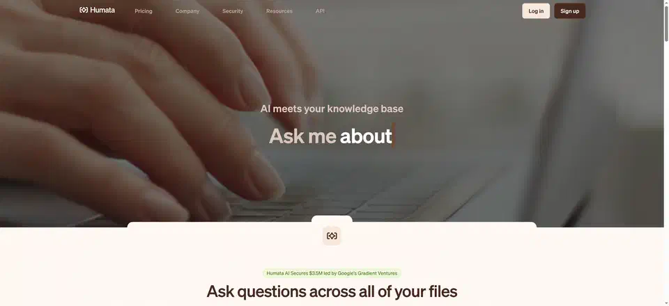 Humata home page headed “AI meets your knowledge base” with an animated “Ask me about” line over a photo of hands typing on a laptop, and a heading below reading “Ask questions across all of your files”