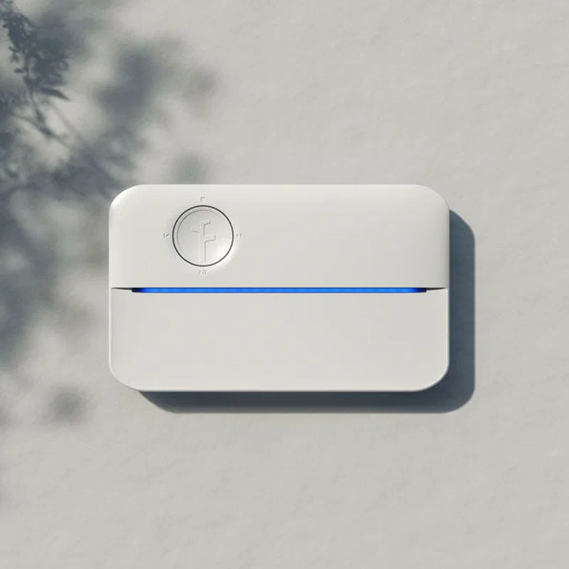 Rachio 3 smart sprinkler controller installed on an exterior wall next to garden landscaping