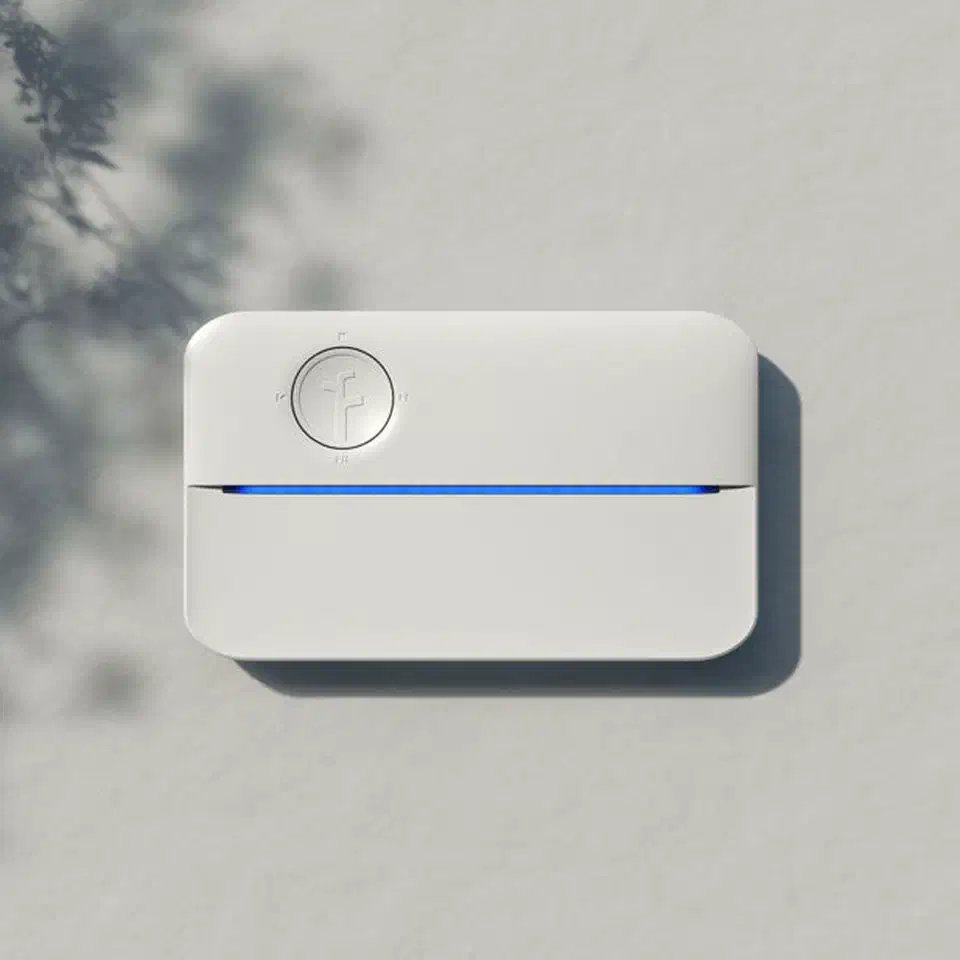 Rachio 3 smart sprinkler controller installed on an exterior wall next to garden landscaping