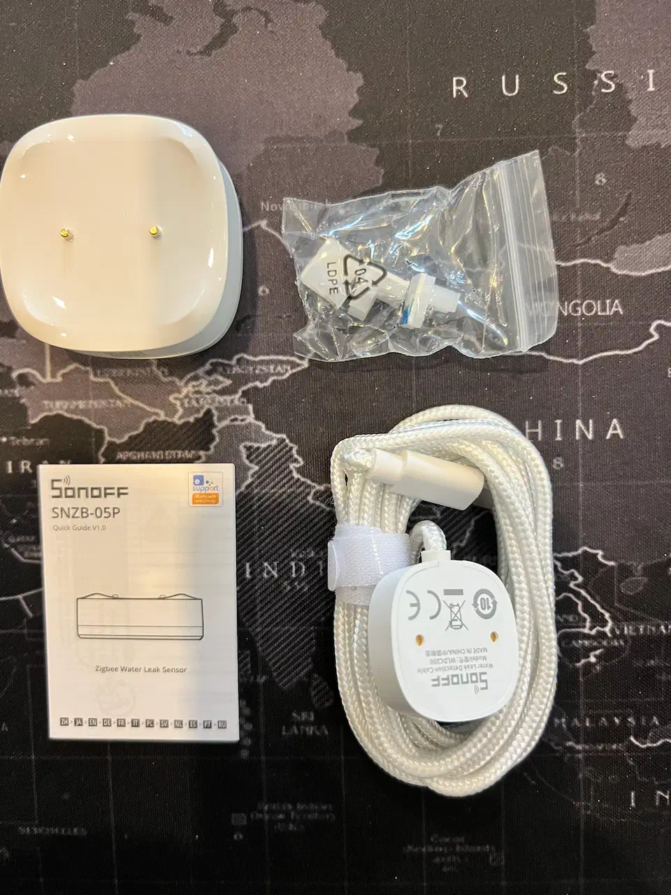 Sonoff SNZB-05P water leak sensor unboxed with its extended detection cable, mounting clips, and manual